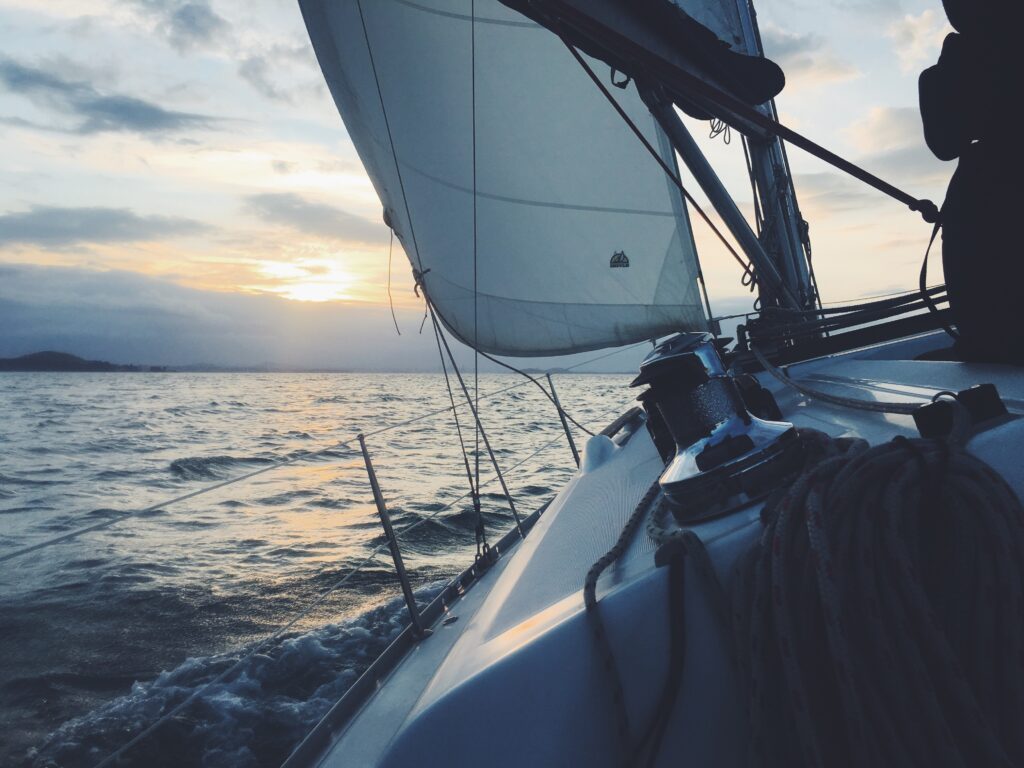 Ein ruhiger Sonnenuntergang vom Deck eines Katamarans aus, mit gesetzten Segeln und sanftem Meeresrauschen, während das Boot durch das Wasser gleitet. ann zu Seekrankheit ade führen und deswegen brauch man ein Pflaster gegen Übelkeit