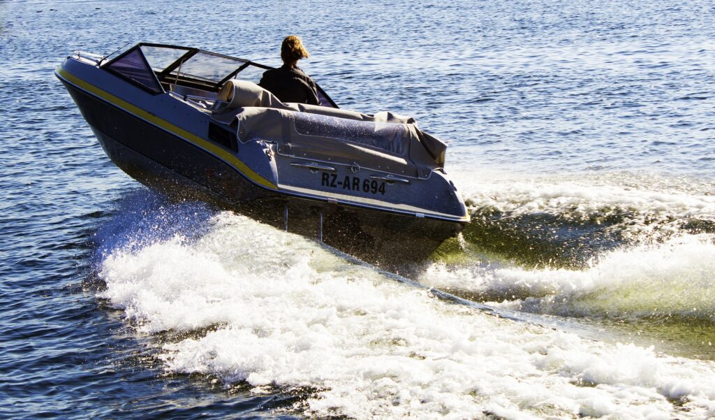 Eine Person mit langen Haaren, die stolz ihr SBF See zur Schau stellt, steuert an einem sonnigen Tag ein Schnellboot mit dem Kennzeichen