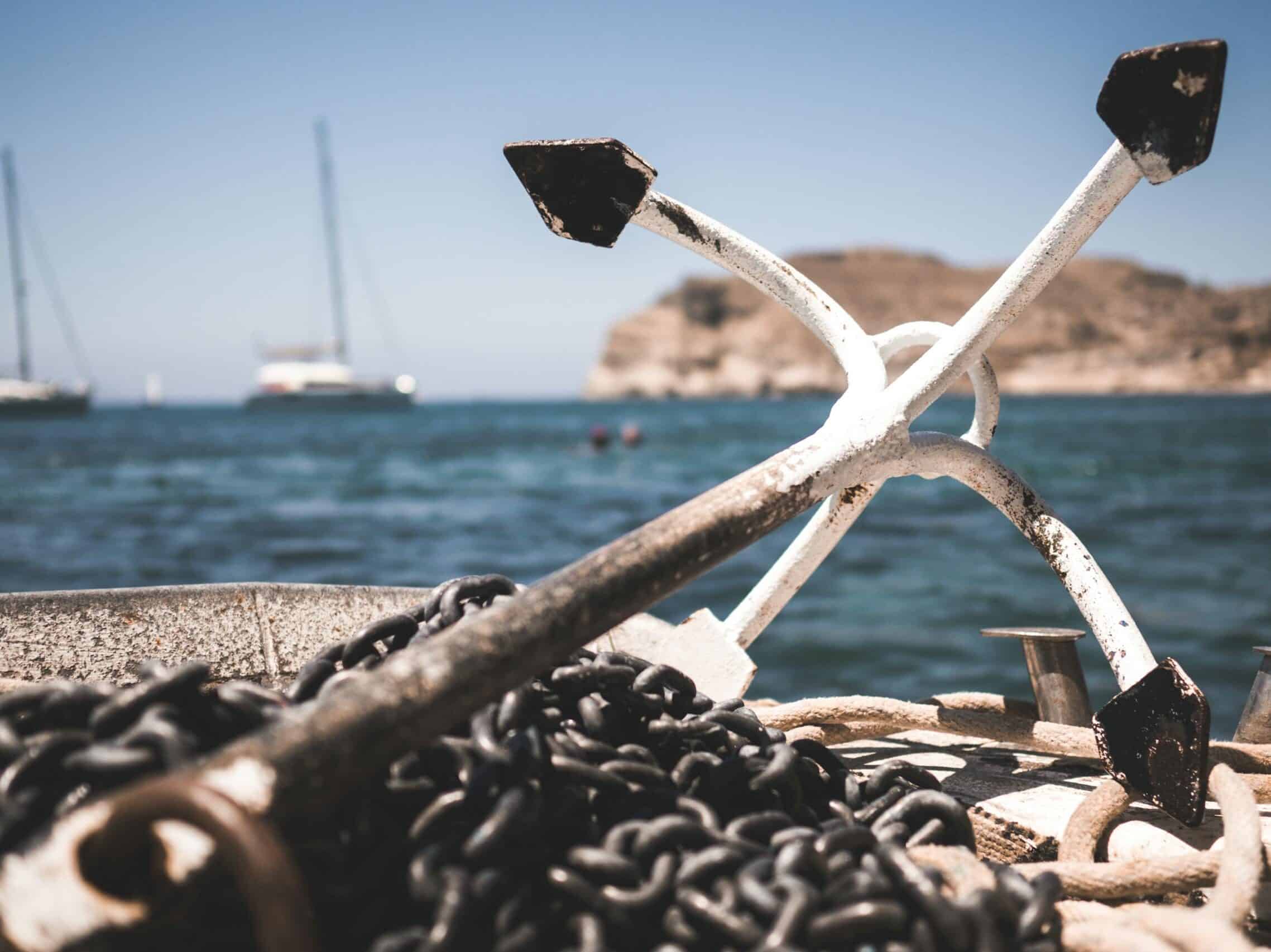 Close-up of boat anchor and chains with ocean and sailboats in the background.