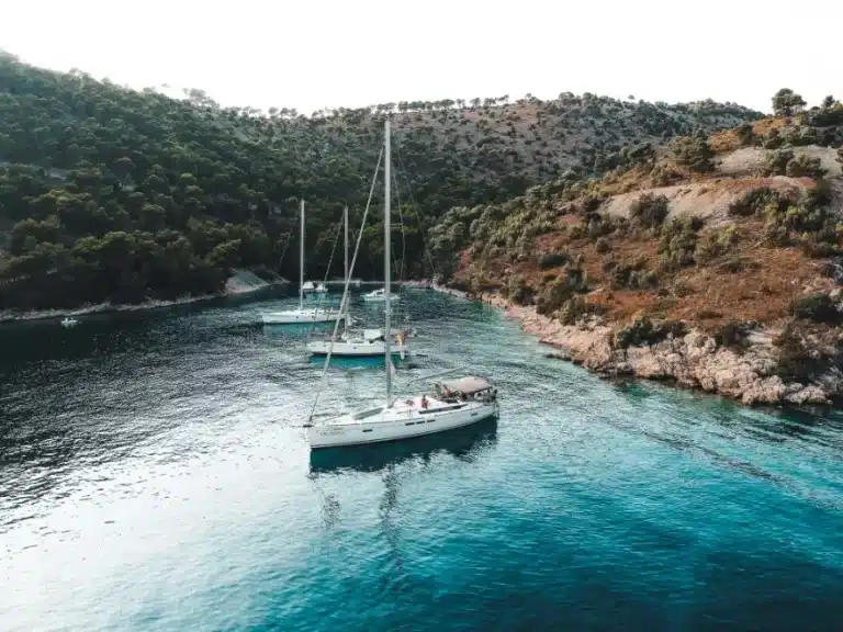 Luftaufnahme von zwei Segelbooten, die in einer ruhigen, abgeschiedenen Bucht vor Anker liegen, umgeben von üppigen grünen Hügeln. Das klare blaue Wasser spiegelt die ruhige und malerische Lage der Segelyacht wider.