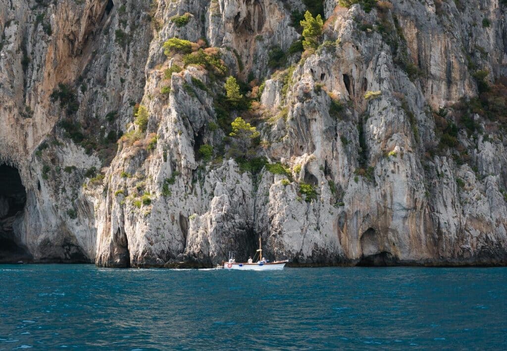 Dominant rocky cliffs of Capri Island with a small boat on the blue ocean waters.