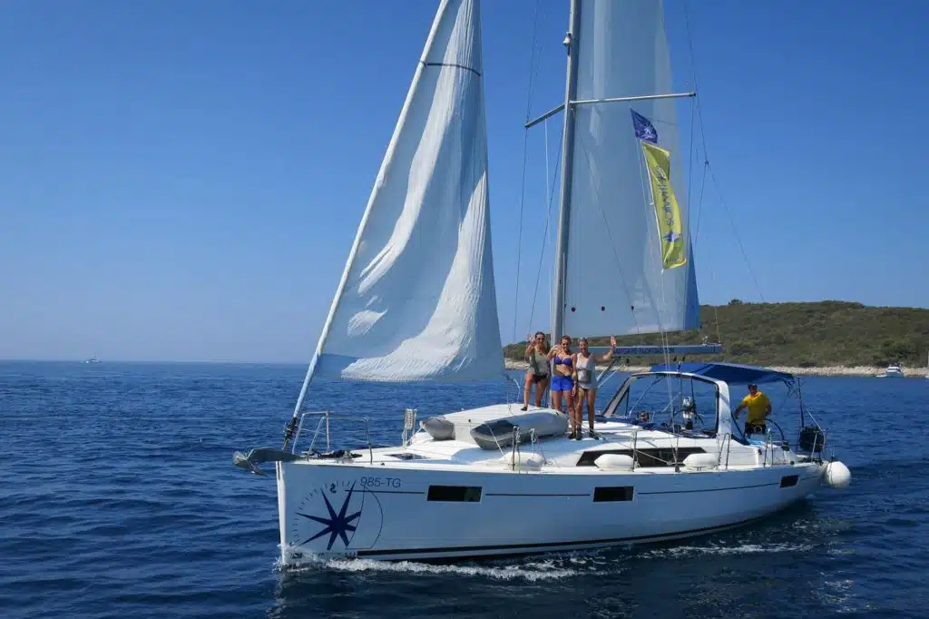 Eine Gruppe von Menschen genießt einen sonnigen Tag auf einer Segelreise mit voll ausgefahrenem Großsegel und Fock auf dem klaren, blauen Wasser.