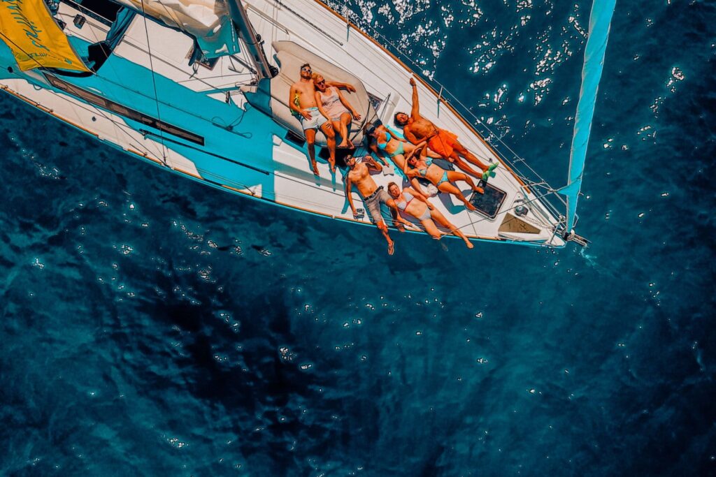 Luftaufnahme einer Gruppe von Menschen, die auf einer im klaren, blauen Wasser treibenden Segelyacht ein Sonnenbad nehmen.